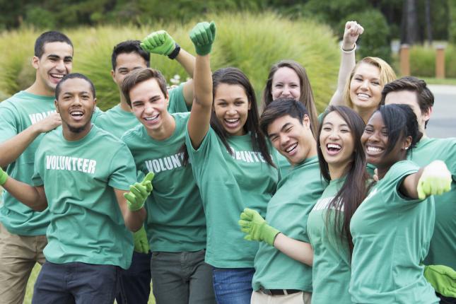 Group of smiling teenagers wearing latex gloves and shirts that read "Volunteer."